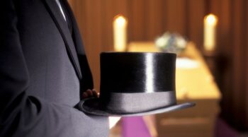 Mão segura uma cartola em cerimônia, representando a função do mestre de cerimônia.