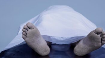 Pés de corpo sob lençol branco em necrotério para explicar o que é rigidez cadavérica.