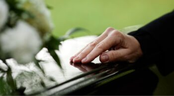 Mão toca carinhosamente a superfície de uma urna envernizada em processos funerários.