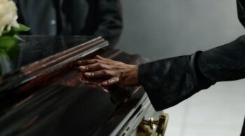 Assistência e cuidado no luto com planejamento funerário familiar Mão sobre um caixão, ressaltando a importância do amparo e do planejamento funerário familiar.