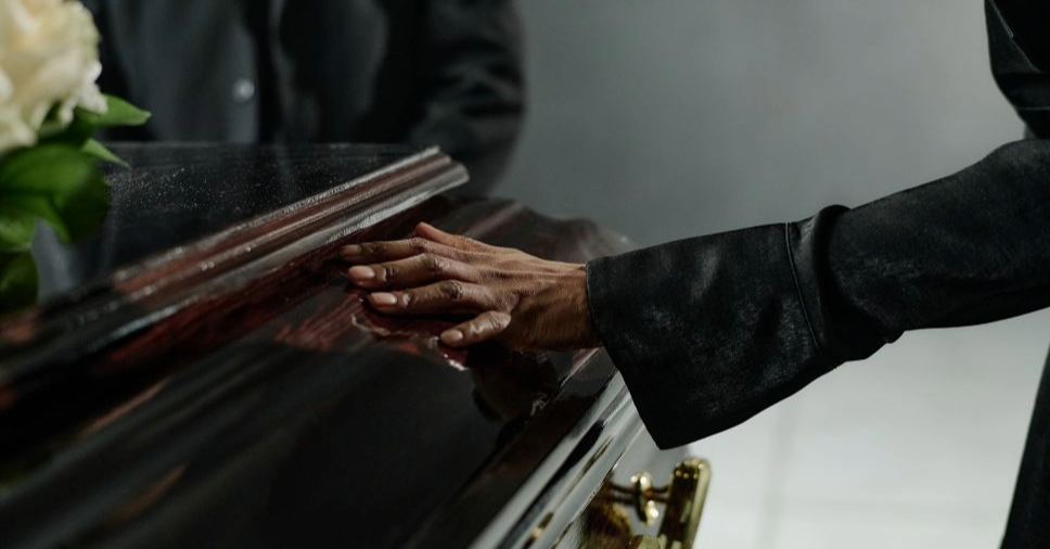 Mão sobre um caixão, ressaltando a importância do amparo e do planejamento funerário familiar.